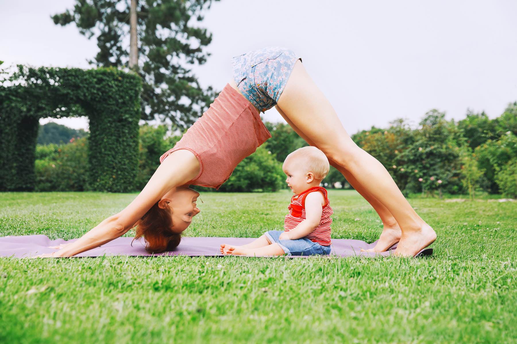 Young woman doing yoga with baby in the summer park. Beautiful mother and daughter like a little buddha exercising on green grass on nature. Family outdoors. Parent with child spend time together. – ©Adobe