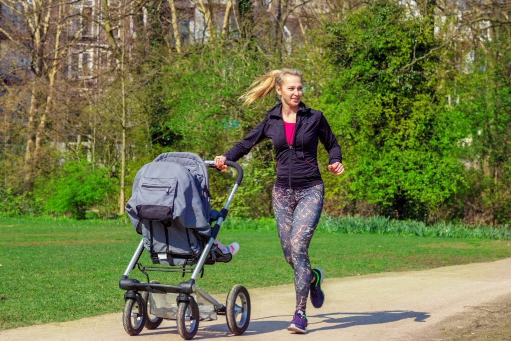 Smiling young woman pushing baby buggy while exercising in a park – ©Adobe